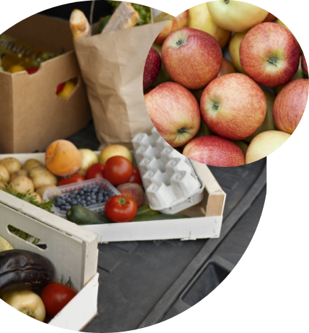 A wooden crate and paper bag filled with assorted fresh fruits and vegetables, including tomatoes, zucchini, and eggs—perfect for pantry food help from Feeding America—with a circular inset showing a close-up of red and yellow apples.