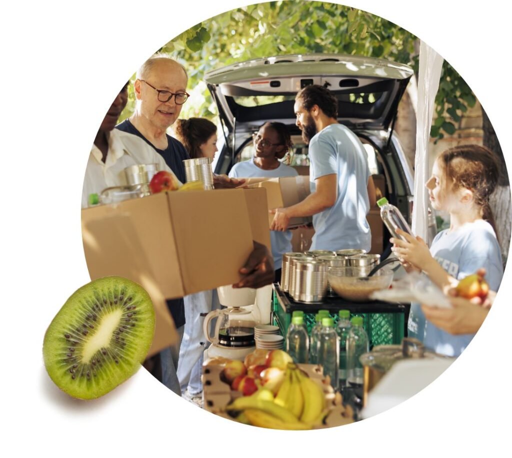 Volunteers distribute food help and drinks from the back of a vehicle outdoors. Fruits, water bottles, and pantry items are visible on a table in the foreground, with a kiwi placed outside the main image circle.
