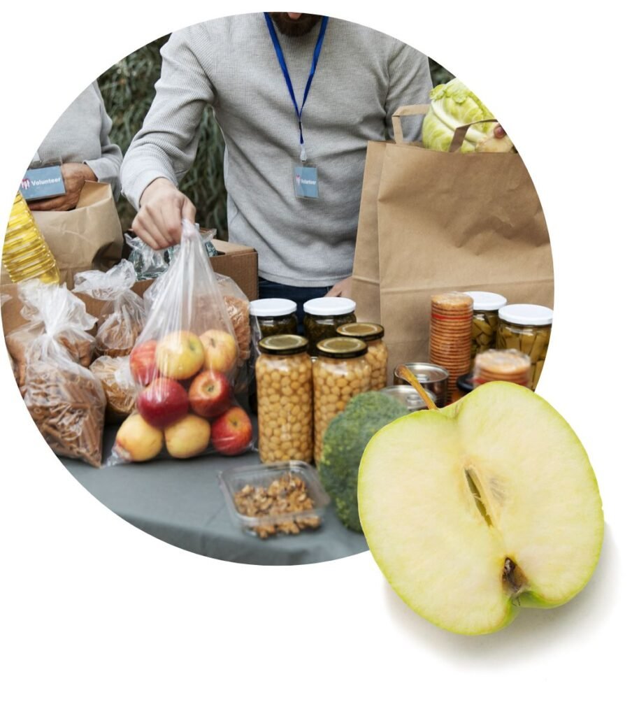 Two people pack groceries—including apples, jars, and bread—on a table, symbolizing the vital work of food banks providing food assistance; a large, sliced green apple is overlaid in the foreground.