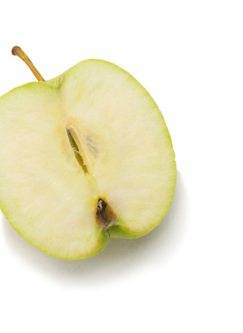 Half of a green apple with the stem attached, showing the seeds and white flesh inside. Placed on a white surface with a visible shadow, this fresh fruit highlights healthy options often provided by food banks like Feeding America.