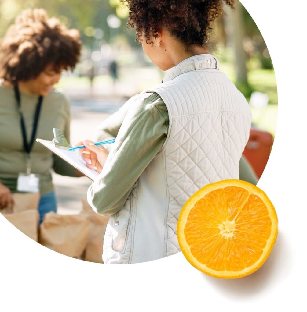 A person wearing a light quilted vest writes on a clipboard outdoors, while another person stands nearby with pantry paper bags. An image of a sliced orange is overlaid in the bottom right corner.